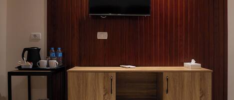 A modern kitchen with a wooden cabinet, a black countertop, a coffee maker, and a TV mounted on the wall.