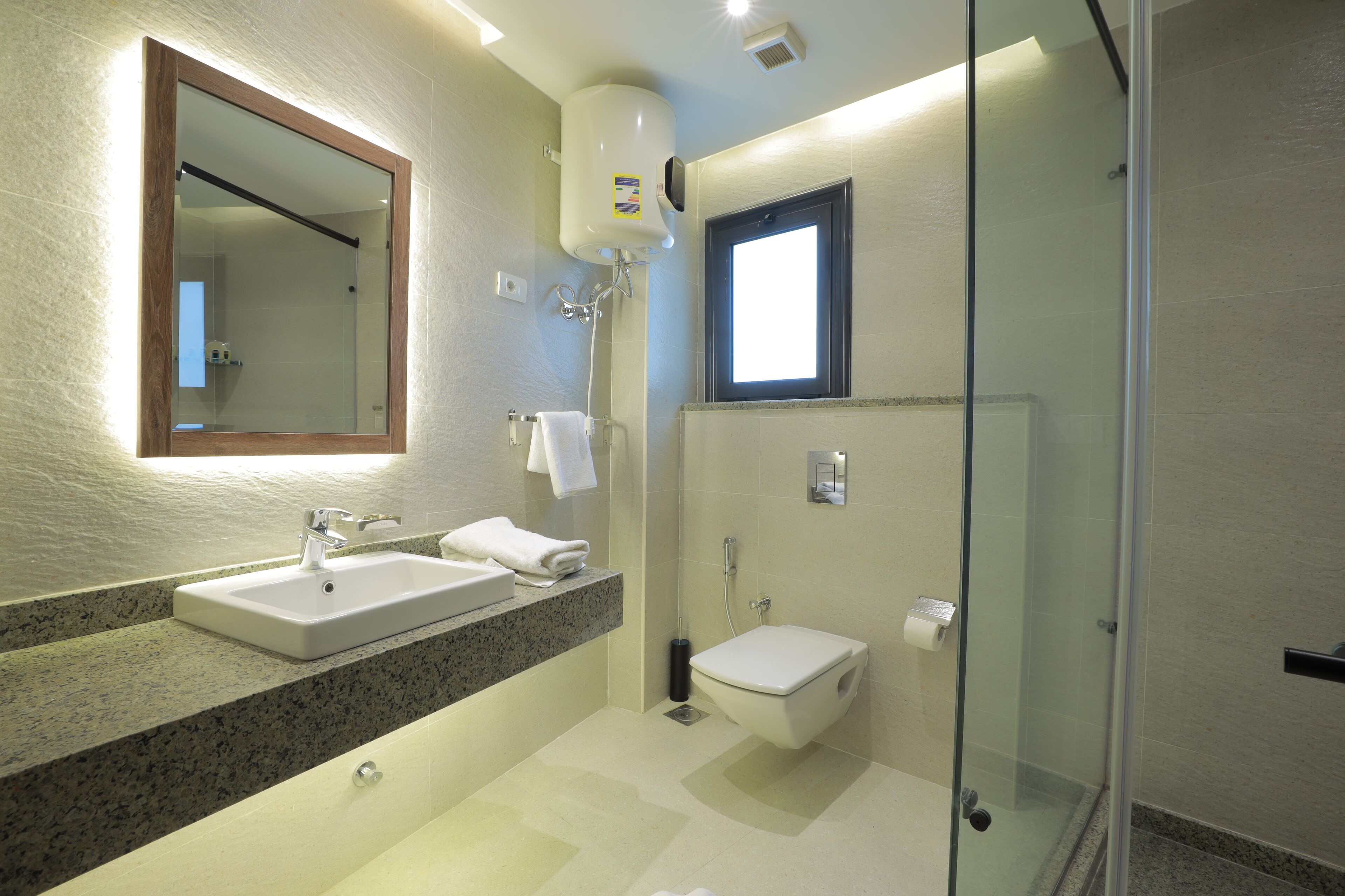 A modern bathroom with a granite countertop, two sinks, a glass shower enclosure, and a small window.