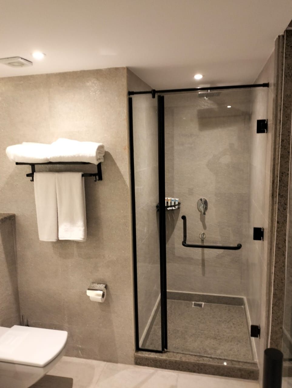 Un bagno moderno con doccia vetrata, lavandino bianco e porta asciugamani con due asciugamani.