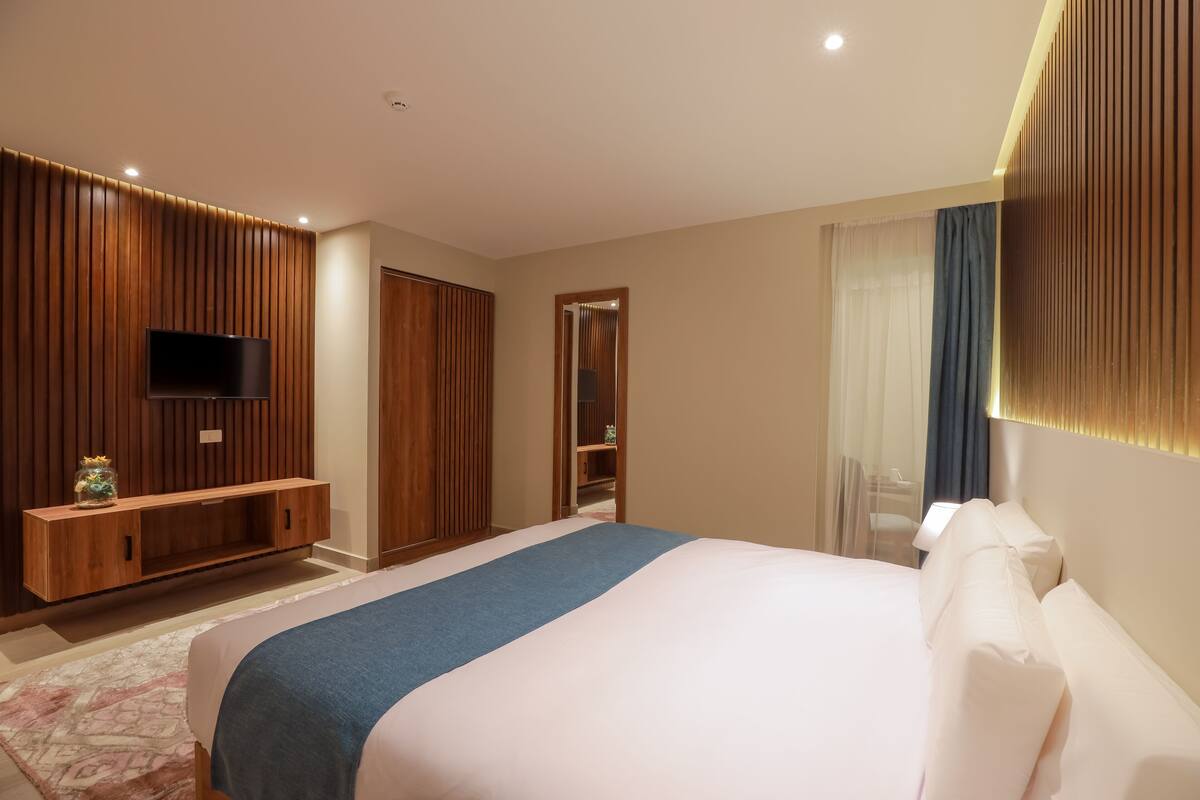 Quarto de hotel moderno com uma cama grande, uma televisão fixada em uma parede de painéis de madeira e um closet espaçoso.