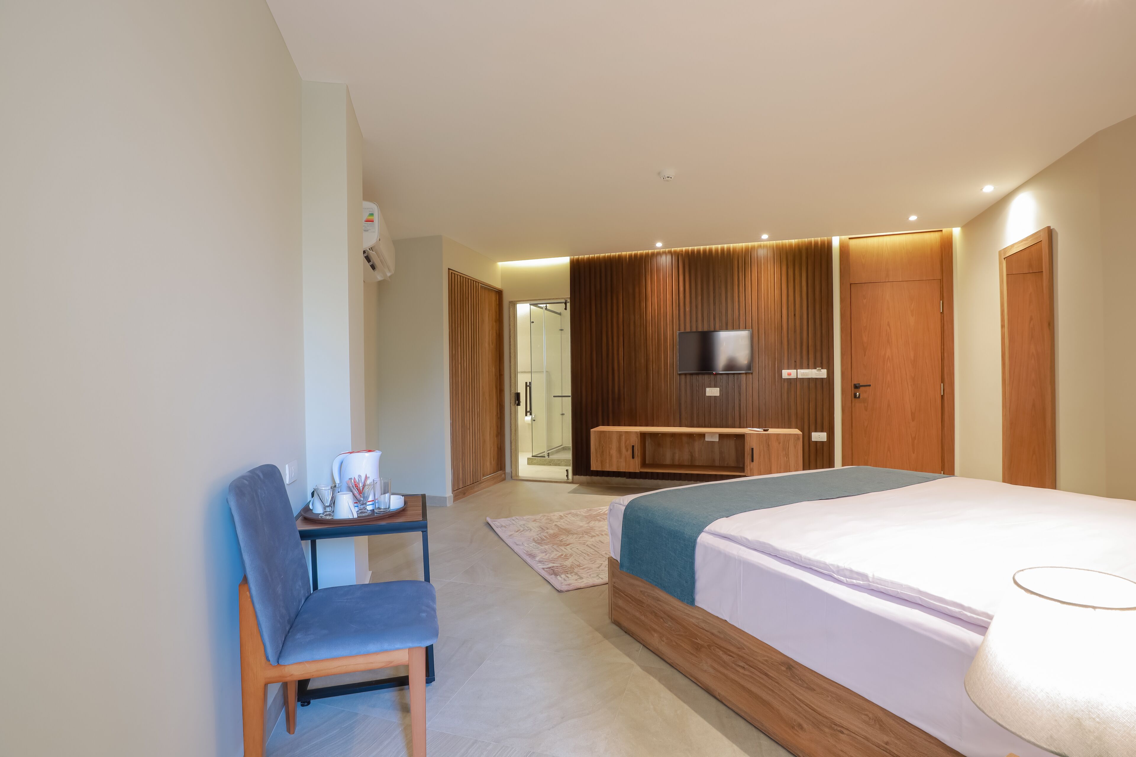 A modern hotel room with a bed, a desk, a chair, a TV, and wooden paneling.