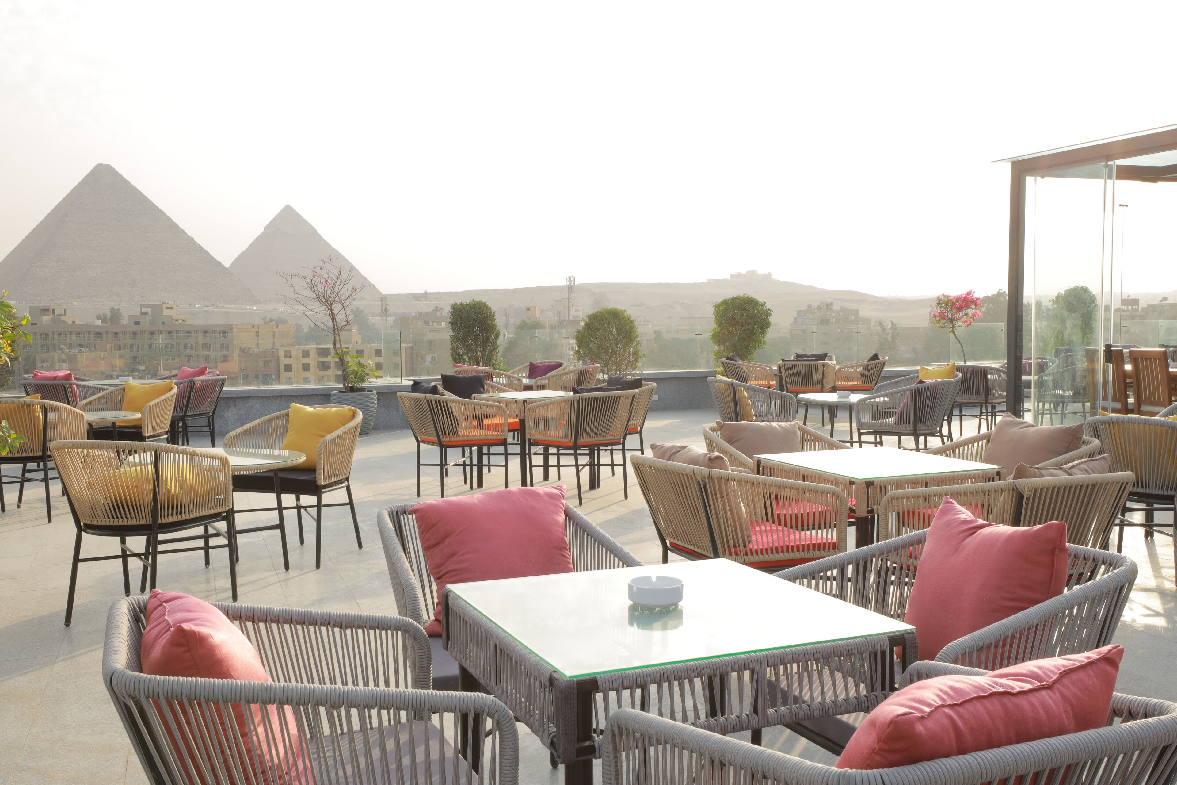 A rooftop terrace with wicker furniture, a glass table, and a view of the pyramids.
