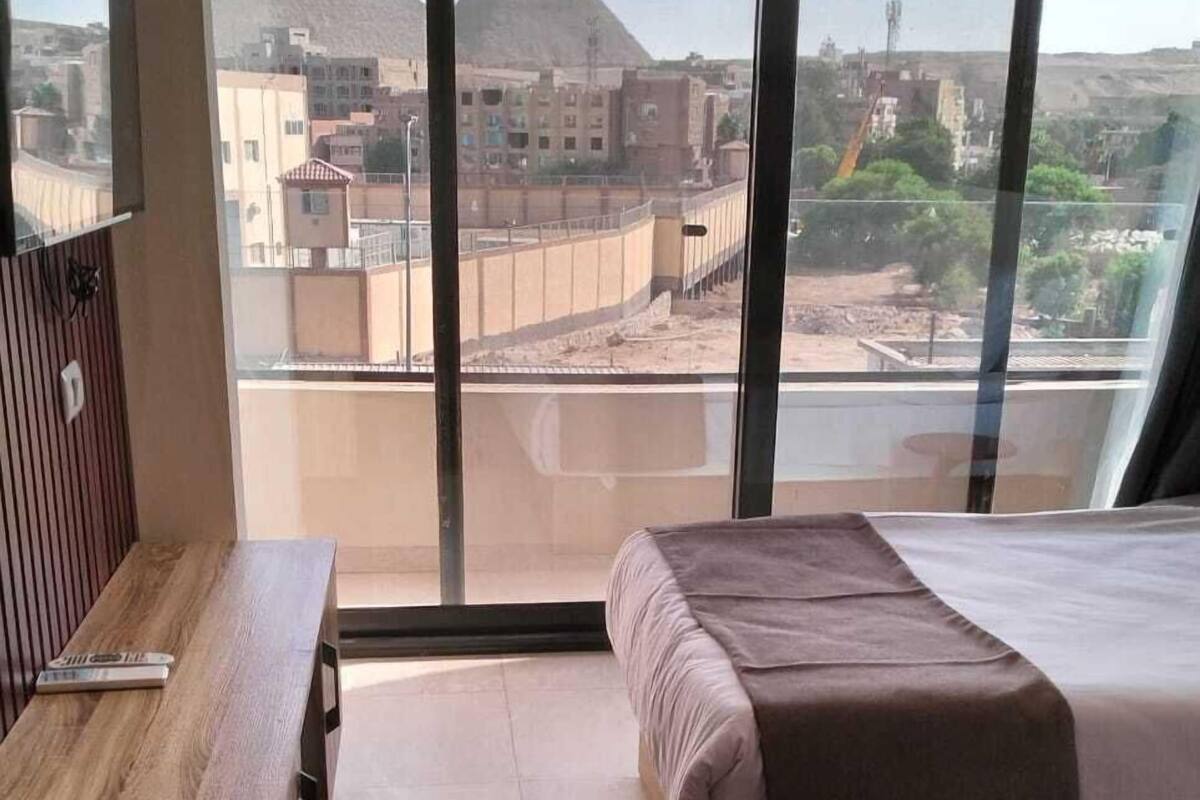 Quarto de hotel moderno com uma grande janela, uma escrivaninha de madeira, uma cama e vista para pirâmides.