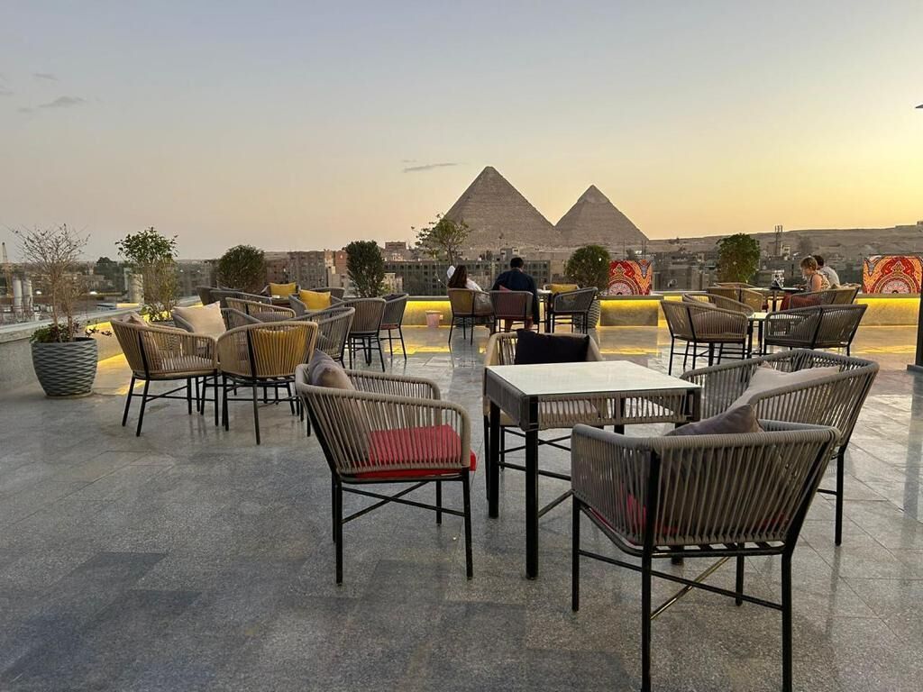 A rooftop terrace with wicker furniture and a view of the pyramids.