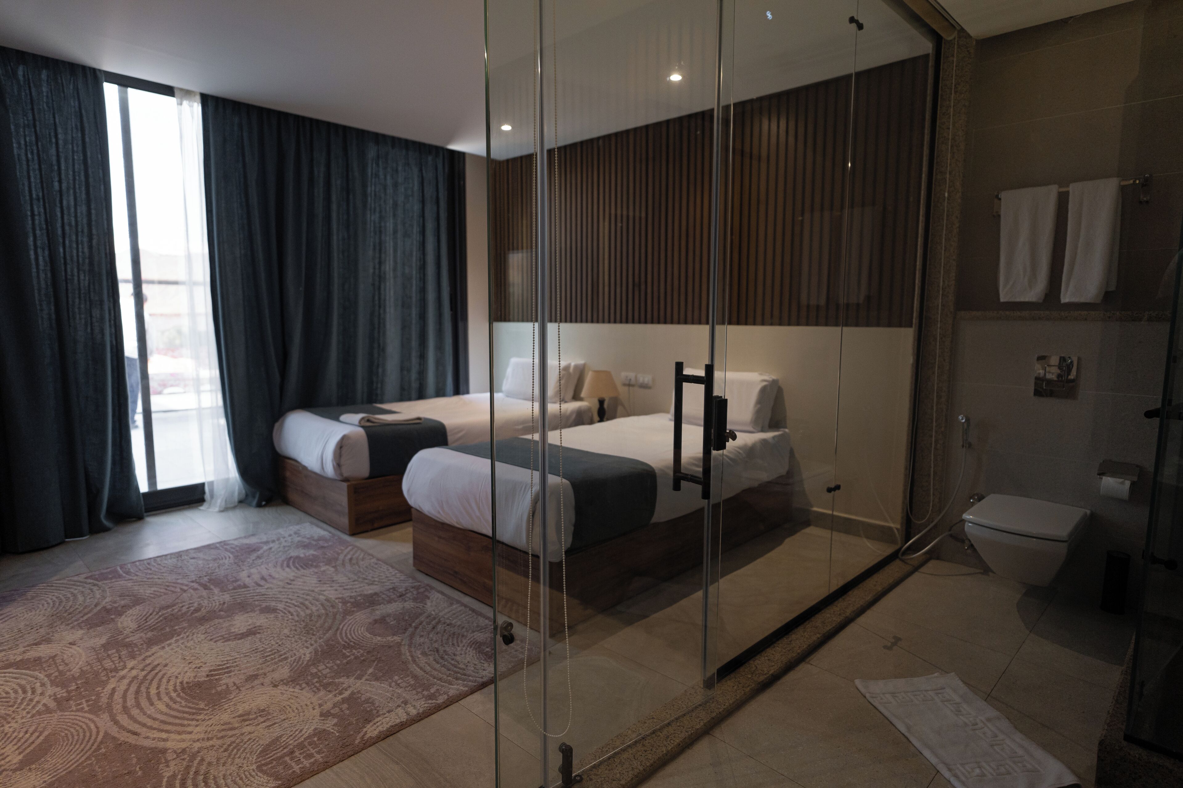 Une chambre d’hôtel moderne dotée d’un grand lit, d’un canapé séparé, d’une cloison en verre, d’un espace douche et offrant une vue sur l’extérieur.