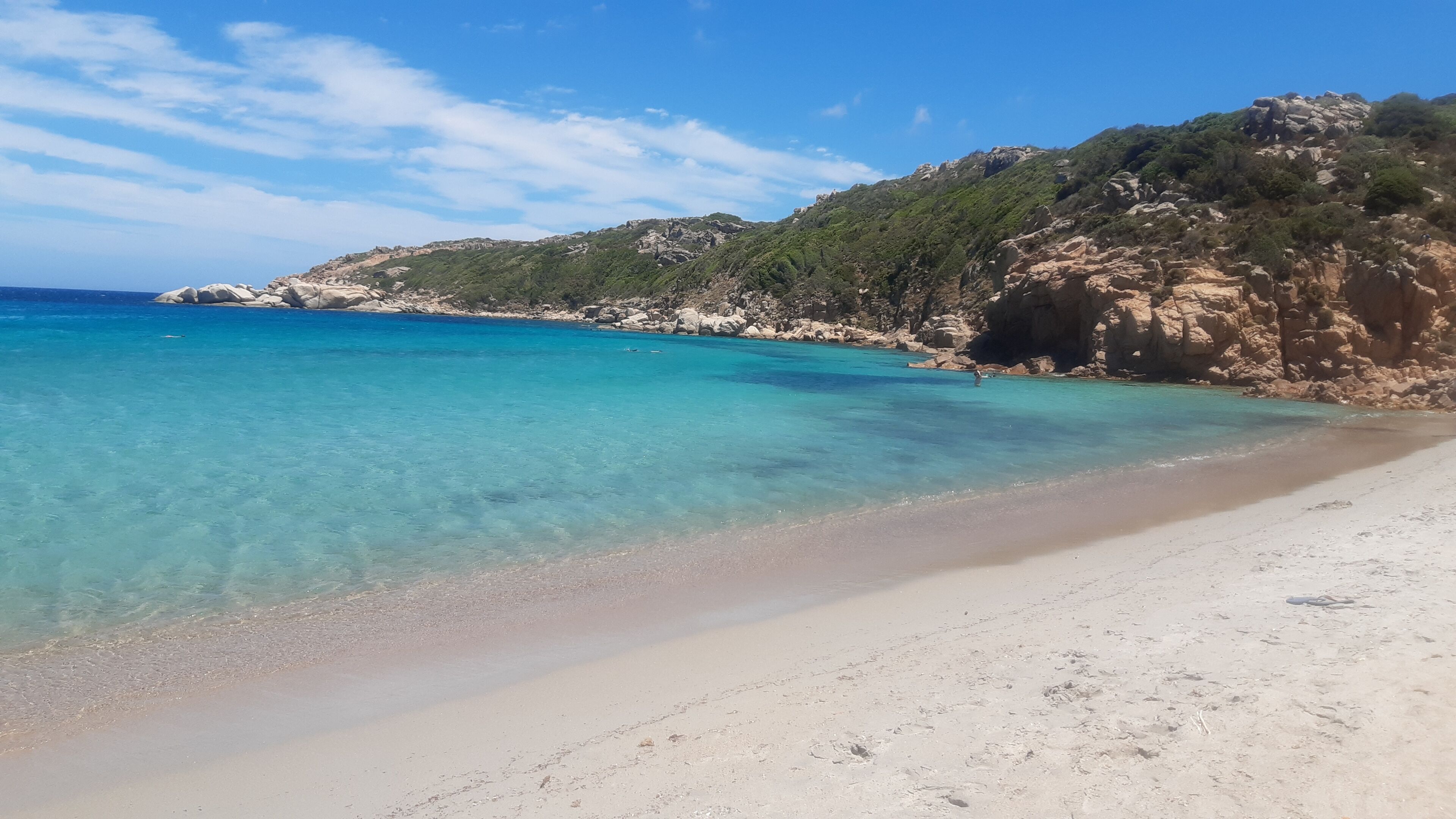 A beach with clear turquoise water, sandy shore, and rocky cliffs.