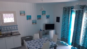 Una cocina compacta con lavamanos, una mesa de comedor con sillas, un televisor sobre un mueble bajo y una ventana con cortinas.