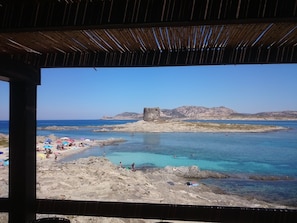 Una playa con aguas turquesas cristalinas, terreno rocoso y una estructura de piedra histórica al fondo.
