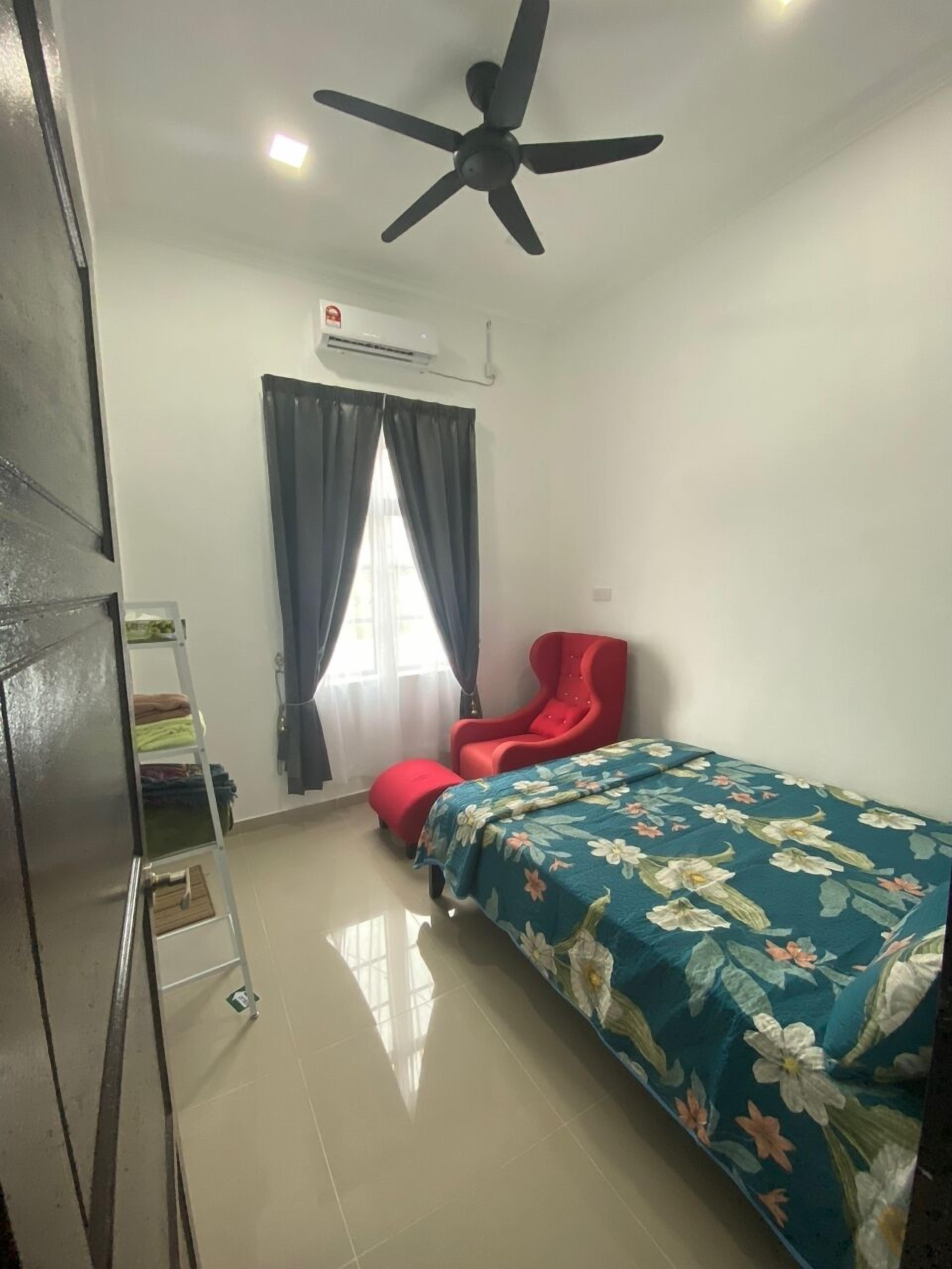 Un dormitorio con cama, una silla roja, ventilador de techo, unidad de aire acondicionado, ventana con cortinas y una escalera de metal.