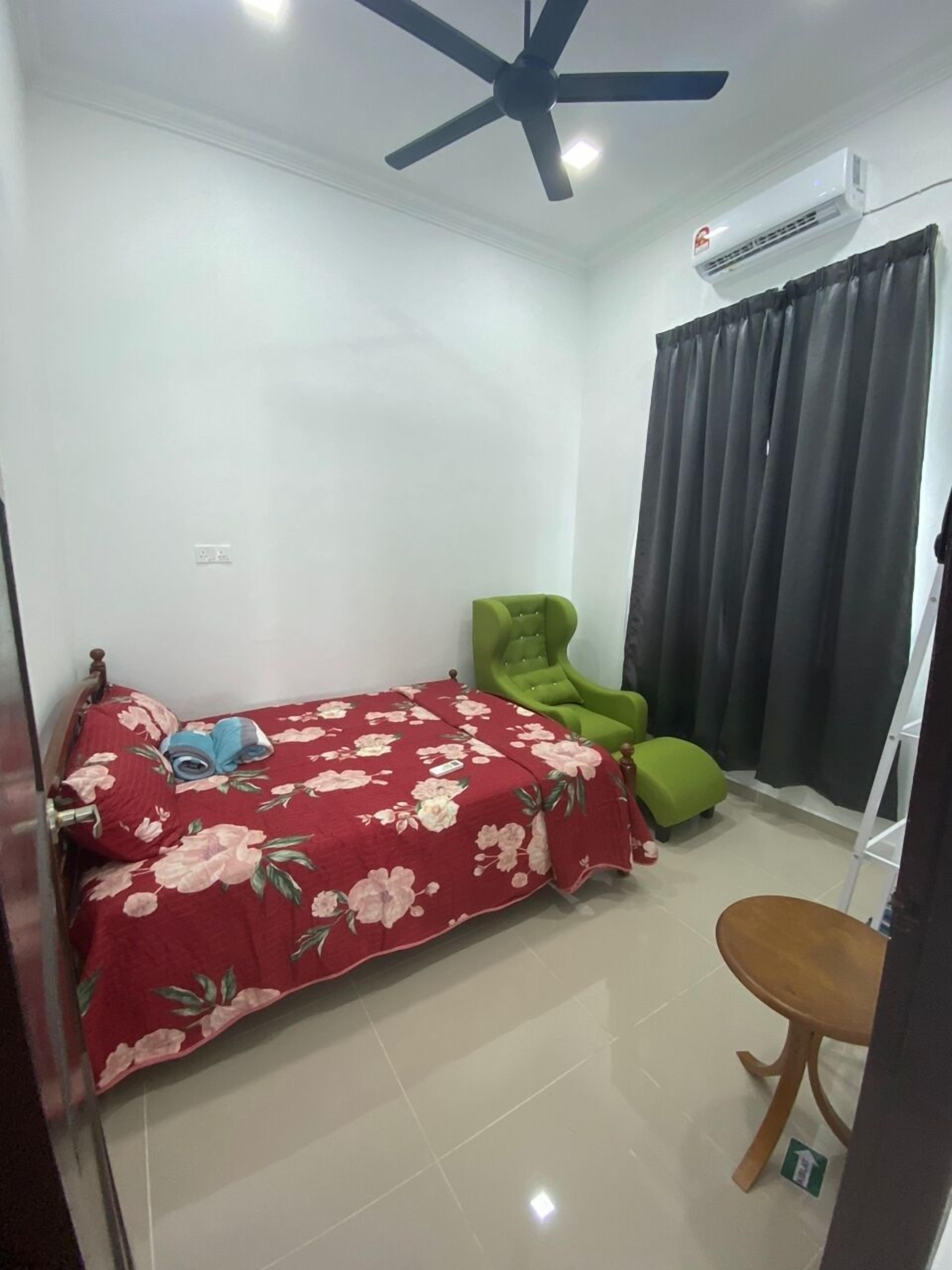 Une chambre à coucher avec un lit, un fauteuil vert, une chaise en bois, un ventilateur de plafond et un appareil de climatisation.