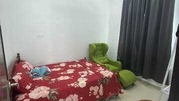 Une chambre à coucher avec un lit, un fauteuil vert, une chaise en bois, un ventilateur de plafond et un appareil de climatisation.