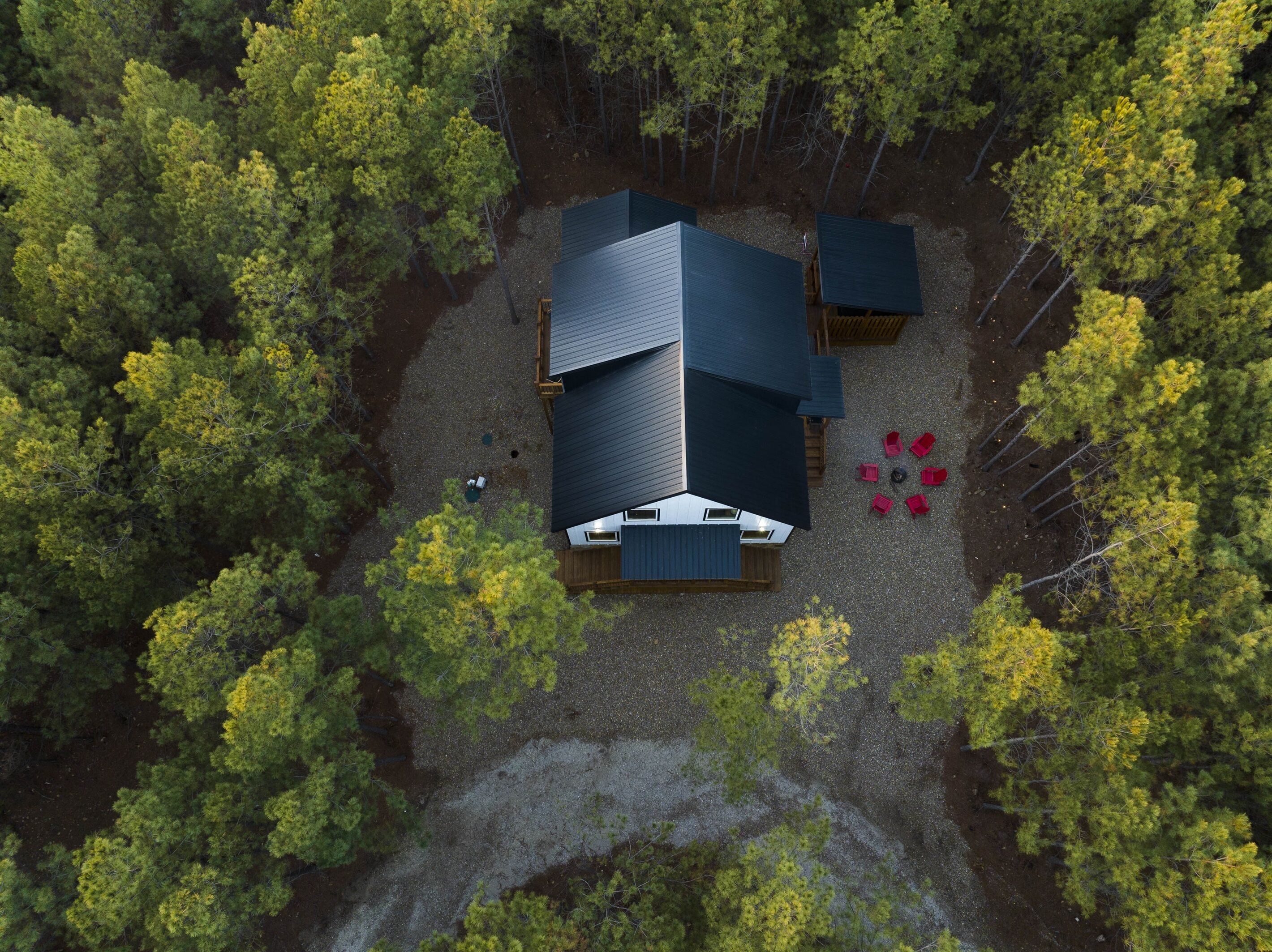 An aerial view of a cabin surrounded by dense forest, with a gravel driveway leading to the entrance.