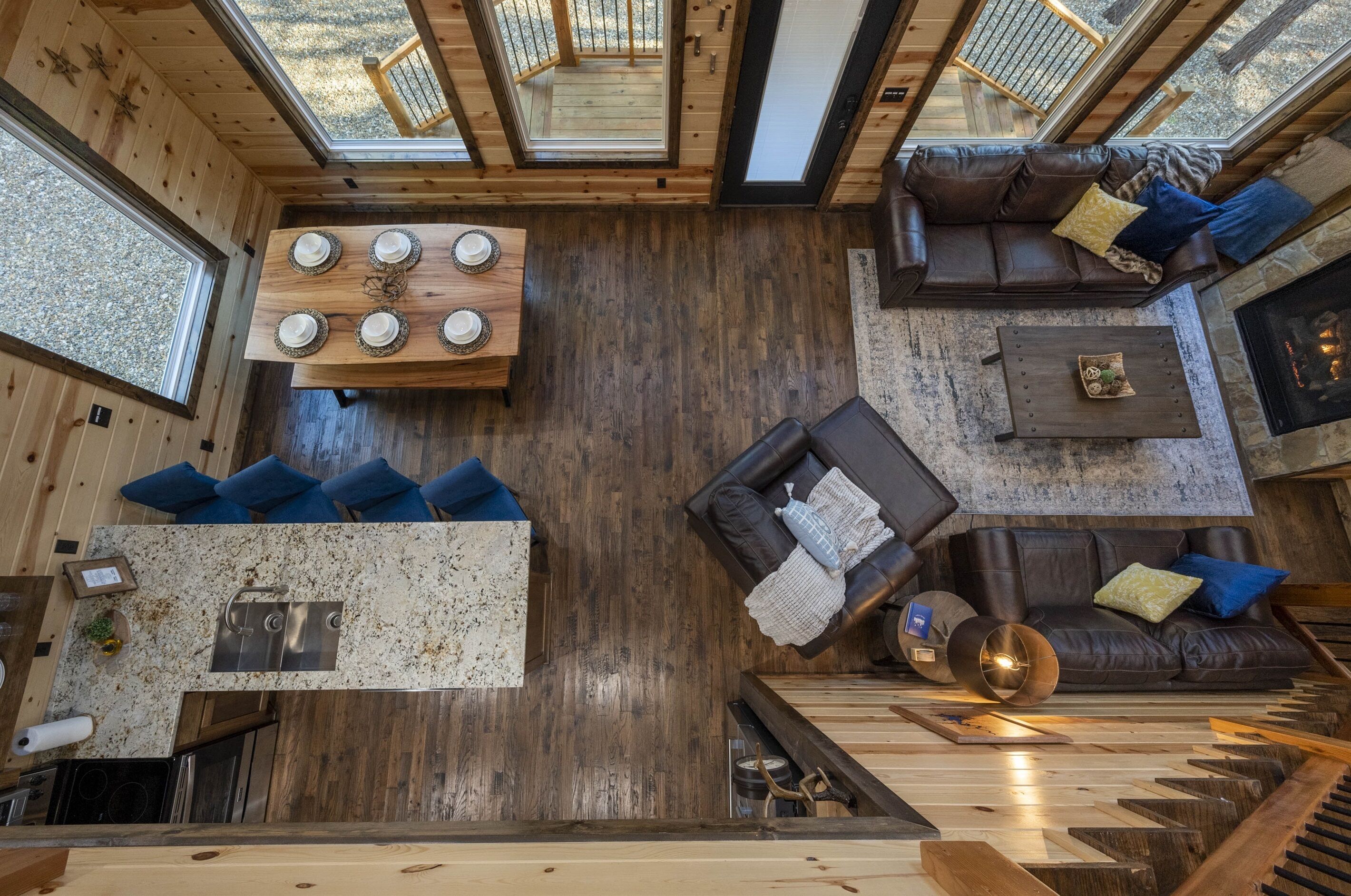 Une pièce spacieuse avec un plancher en bois, une table à manger avec quatre assiettes, un canapé avec des coussins, une cheminée et une grande fenêtre.