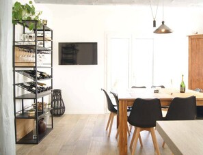 Un coin repas comprenant une table en bois, des chaises noires, une étagère en métal avec des verres et un buffet en bois.