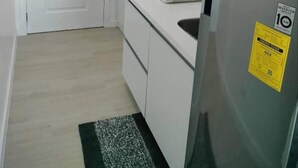 Eine kleine Küche mit weißen Schränken, einem Edelstahlkühlschrank und einer Mikrowelle.