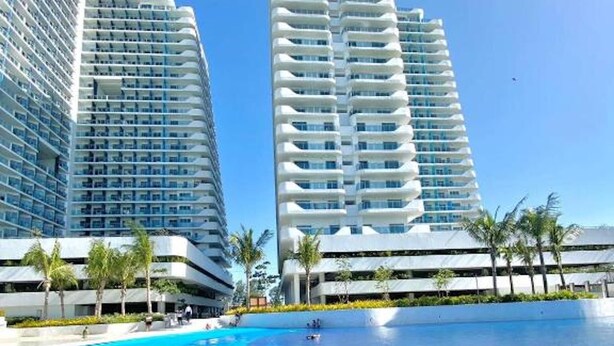 Ein modernes Hotel mit großem Schwimmbad, mehreren Balkonen und blauem Himmel.