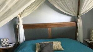 A bedroom with a bed under a canopy, a wooden headboard, and a nightstand with a checkered pillow. - AZUR bungalow in the heart of a quiet, leafy garden (LE MOULE)