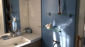 A bathroom with a white sink, a mirror, and two glass shelves with toiletries. - AZUR bungalow in the heart of a quiet, leafy garden (LE MOULE)