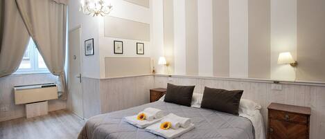 A hotel room with a bed, a nightstand, a wall-mounted air conditioner, and a window with curtains.