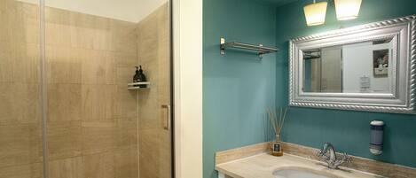 A bathroom with a glass shower enclosure, a sink with a mirror, and a wall-mounted light fixture.
