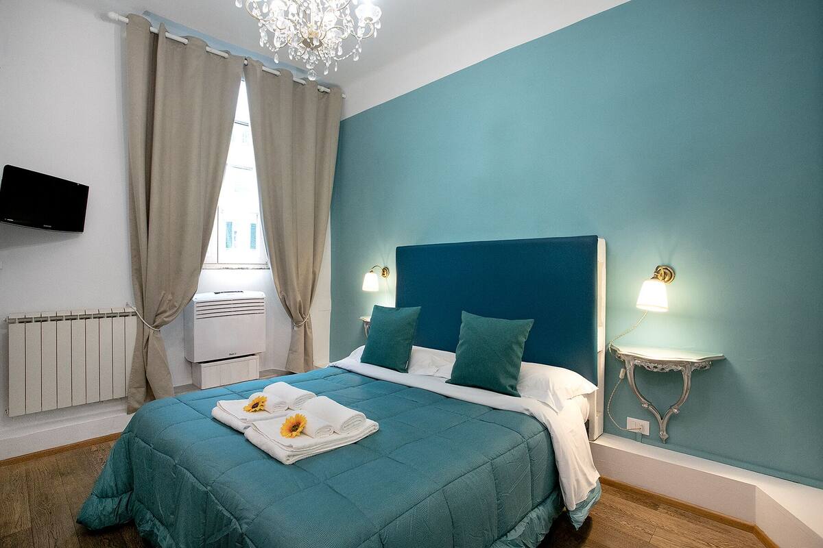 A bedroom with a teal bedspread, a white headboard, and two bedside lamps.