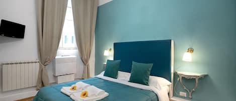Un dormitorio con colcha color turquesa, cabecero blanco y dos lámparas de noche.