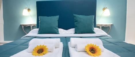 A neatly made bed with teal bedding, two pillows, and two towels with sunflowers.