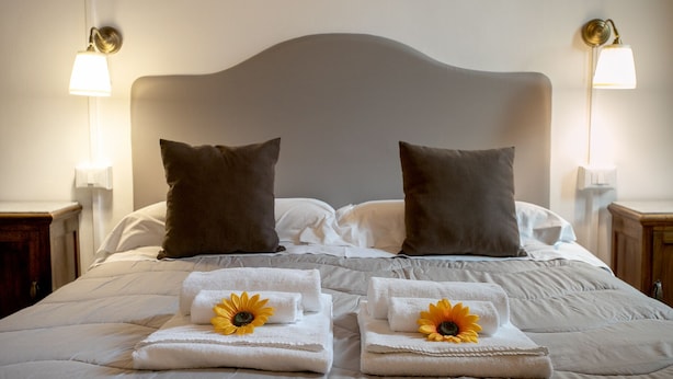 A neatly made bed with two pillows, two folded towels with sunflowers, and bedside lamps. - Residenza Centro Storico (Lucca)