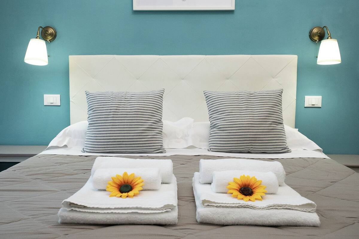 A bed with a white headboard, two striped pillows, and two towels with sunflowers.