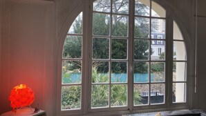 Une pièce dotée d’une grande fenêtre en arc de cercle, d’un canapé avec des coussins et d’une table avec une lampe.