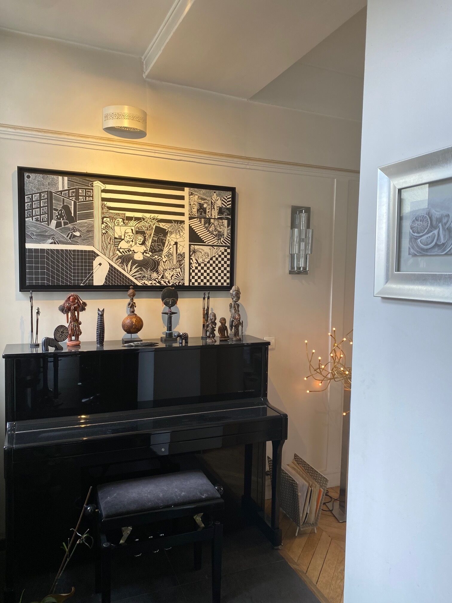 Ein schwarzes Klavier mit dazugehöriger Bank, darüber ein großes Schwarz-Weiß-Kunstwerk und ein gerahmtes Bild an der rechten Wand.