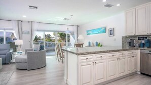 Een moderne keuken met witte kasten, een granieten aanrechtblad en een eethoek met een grijze bank en stoelen.