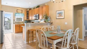 A kitchen with wooden cabinets, a central island, a dining table with chairs, and a chandelier. - Ginger Mermaid / 916 E Dolphin Drive (Oak Island)