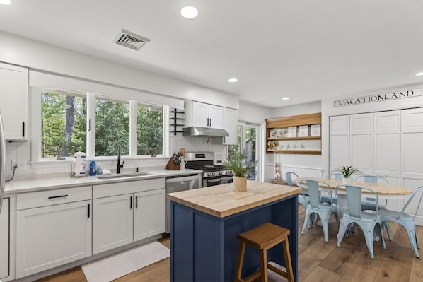 A modern kitchen with white cabinets, a central island, and a dining area with light blue chairs.