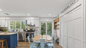 A modern kitchen with white cabinets, a wooden dining table, and light blue chairs. - SAUNA & GAME ROOM- Pet friendly! Close to Dock Square and the Beach! (Kennebunk)