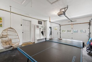 A ping pong table in a garage with a hanging chair, a coat rack, and a sign that says 'MAINE.'