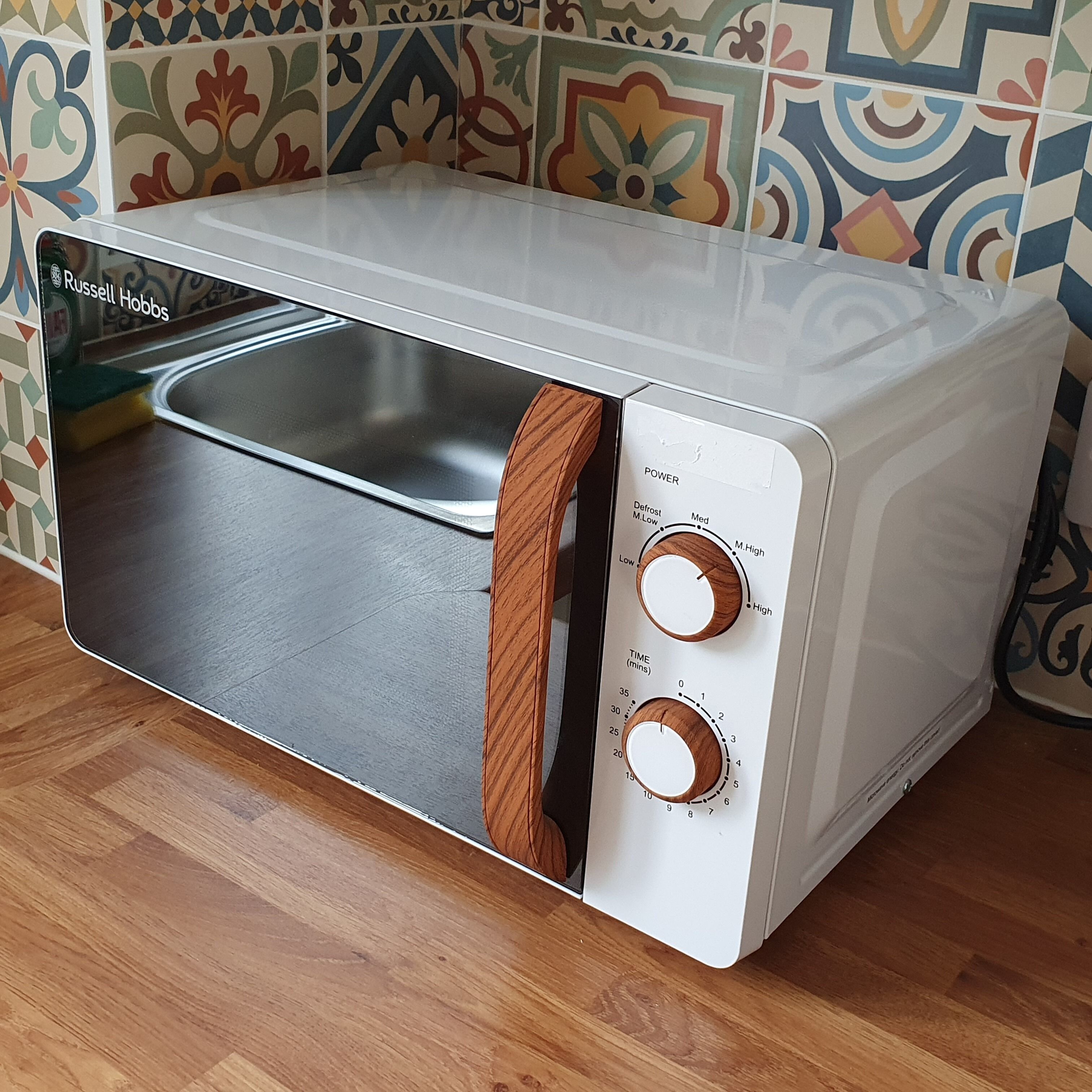 A white microwave with wooden handles and a stainless steel interior, placed on a wooden floor.