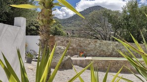 A stone wall with a bench, a small table, and a painting in a garden setting with mountains in the background. - Maison Neuve 6 Personnes Monticello (Monticello)