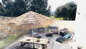 An outdoor patio with a thatched umbrella, wicker furniture, a stone wall, and a view of trees and hills. - Maison Neuve 6 Personnes Monticello (Monticello)