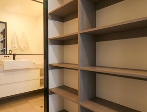 Un baño moderno con lavamanos blanco, espejo y estantes de madera.