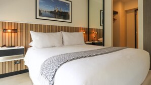 A hotel room with a large bed, a wooden headboard, two bedside tables with lamps, a framed picture on the wall, and a mirror on the door.