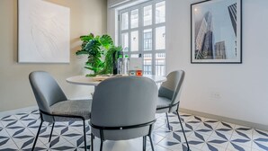 Een moderne eetruimte met een ronde tafel, twee grijze stoelen, een potplant en een stadsgezicht schilderij.