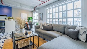 Een moderne woonkamer met een grijze bank, een glazen salontafel en uitzicht op de stad door grote ramen.