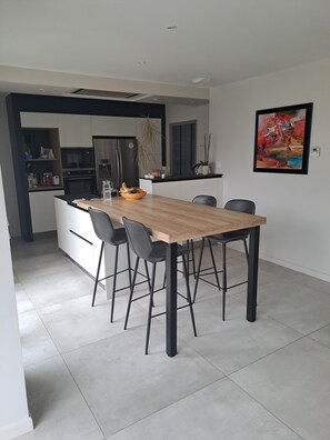 Een moderne keuken met een eethoek, met een houten tafel, zwarte stoelen en een koelkast.