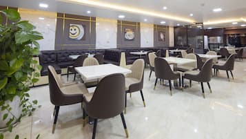 Un intérieur de restaurant moderne avec un sol en marbre, des banquettes noires et beige recouvertes de tissu et des tables blanches.