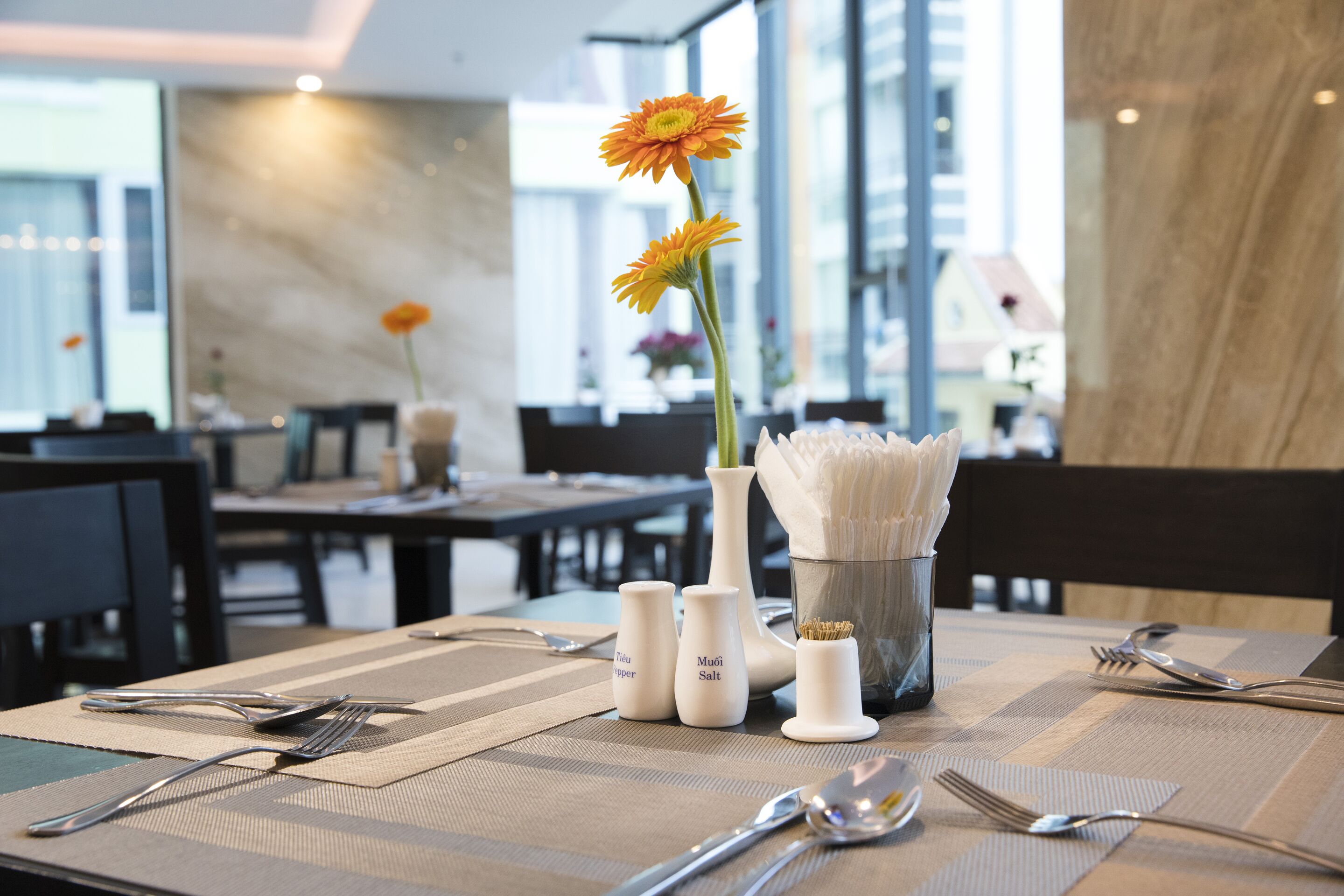 A dining table set with utensils, salt and pepper shakers, and a vase with a single flower.