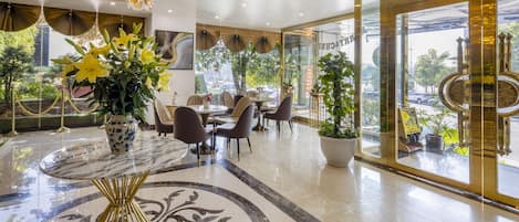 Eine moderne Hotellobby mit einer Marmorrezeption, gemütlichen Sitzgelegenheiten, großen Fenstern und einem Kronleuchter.