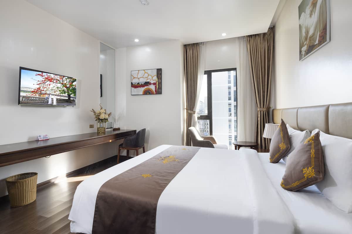 Habitación de hotel con una cama grande, un escritorio, una silla, un televisor y una ventana con cortinas.