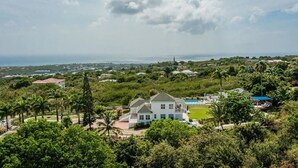 En stor bolig med swimmingpool, omgivet af frodig vegetation og havudsigt.