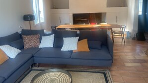 A modern living room with a dark blue sectional sofa, a wooden dining table, and a kitchen area in the background.